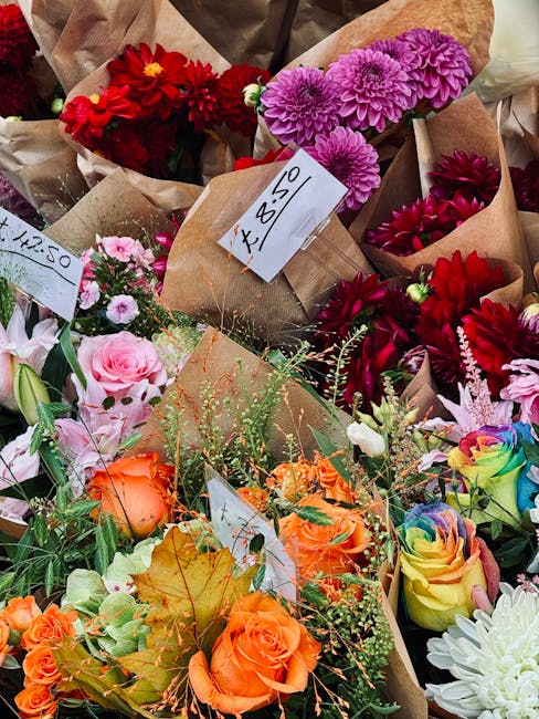 A vibrant assortment of freshly arranged flowers at a market stall, featuring deep red dahlias, bright pink chrysanthemums, pastel pink roses, orange roses, and multicolored rainbow roses, all wrapped