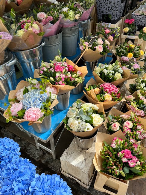 A display of fresh flower bouquets arranged in small metal buckets and wrapped in brown kraft paper, featuring a variety of blooms such as pink roses, white lisianthus, pale green hydrangeas, and past