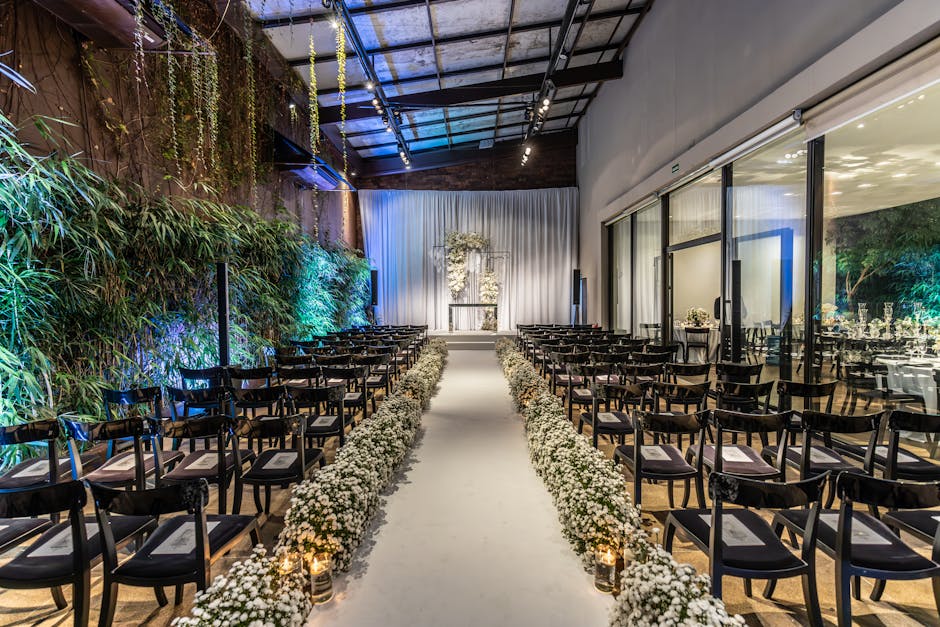 A beautifully arranged indoor wedding ceremony space at a venue in Deptford Dockyard, featuring a central aisle decorated with white baby's breath flowers lining both sides. The aisle leads to a small